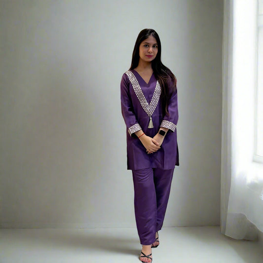 Woman in a purple traditional outfit standing in front of a patterned curtain.